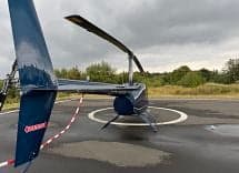 A blue Robinson R44 helicopter on a helipad, viewed from the rear.