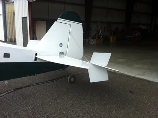 The tail section of a white and green aircraft is parked in a hangar.