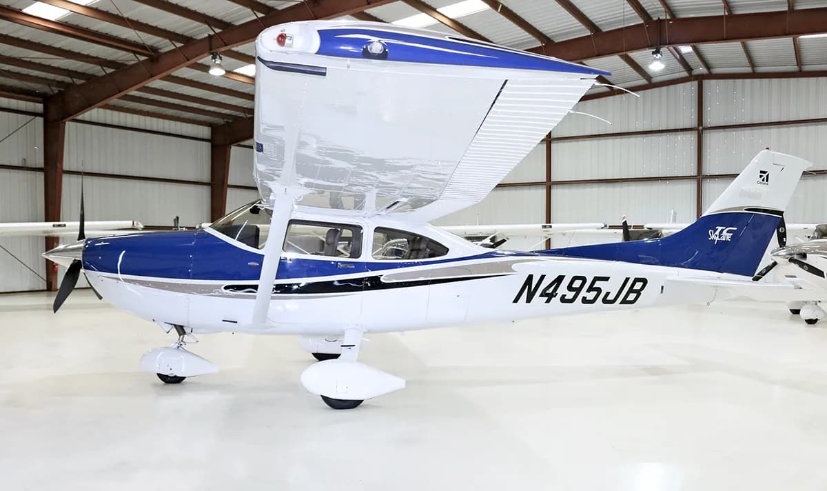 A white and blue single-engine propeller aircraft, N495JB, with its wing up, parked in a hangar.