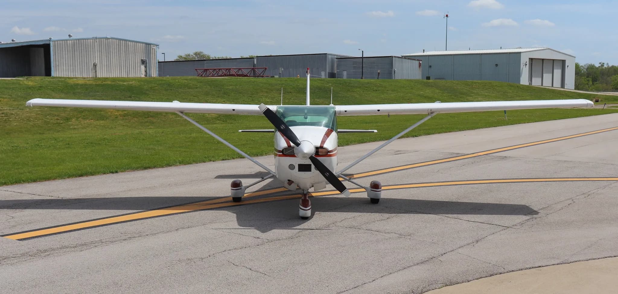 A head-on view of the Cessna Skylane S (N759RR) on an airfield with hangars in the background.