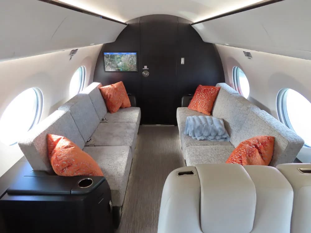 Aircraft cabin with couches and orange pillows.