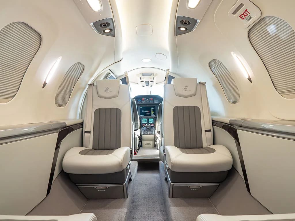 The interior cabin of a HondaJet, with light grey and white leather seats, looking directly into the cockpit.