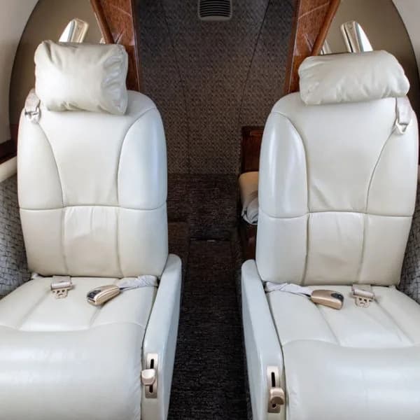 A close-up view of two light beige leather aircraft seats with seatbelts.
