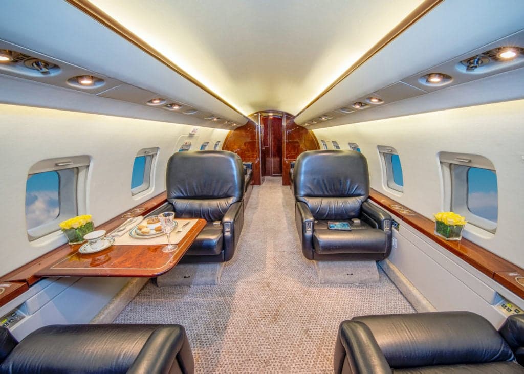 View of the Challenger aircraft interior with a leather seat and table setting.
