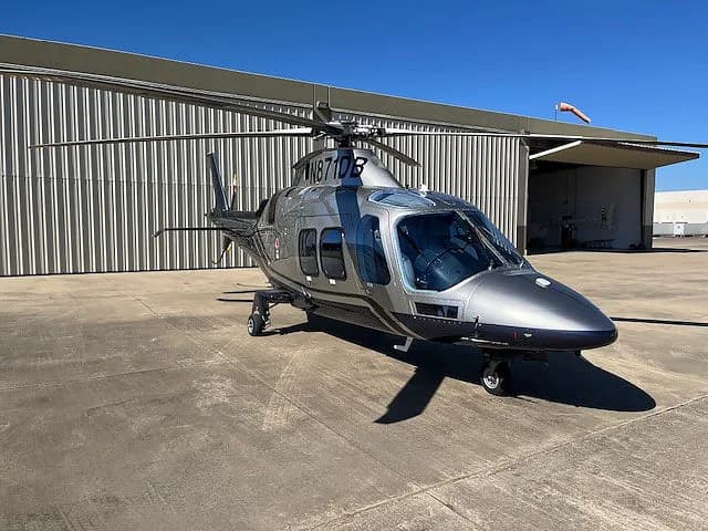 Front quarter view of a silver and gray AgustaWestland AW109SP helicopter on the ground.