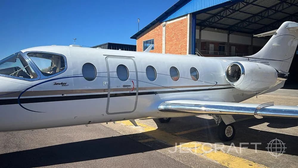 A close-up side view of a white Hawker 800XP business jet parked in front of a hangar.