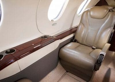 A single leather seat in the Citation CJ3+ cabin is next to a wood-trimmed side console with cupholders.