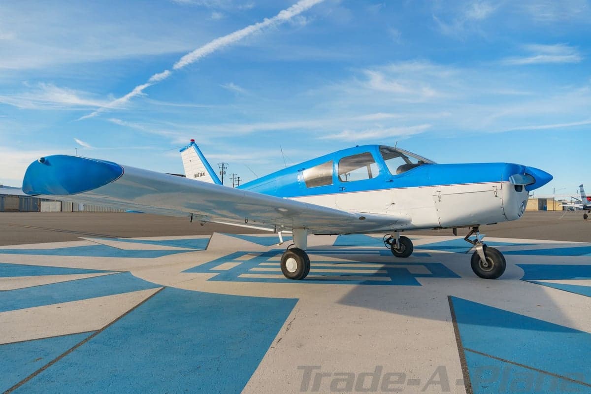 A side view of the blue and white single-engine aircraft N8718N under a clear blue sky with contrails.