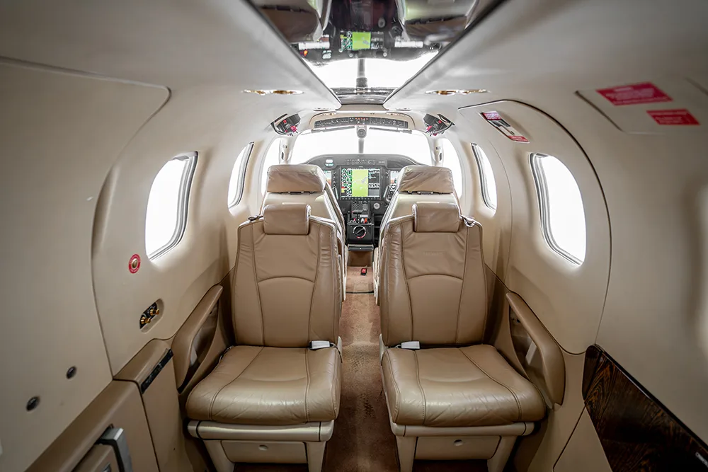 A view from the aircraft cabin looking forward into the cockpit with beige leather seats in the foreground.