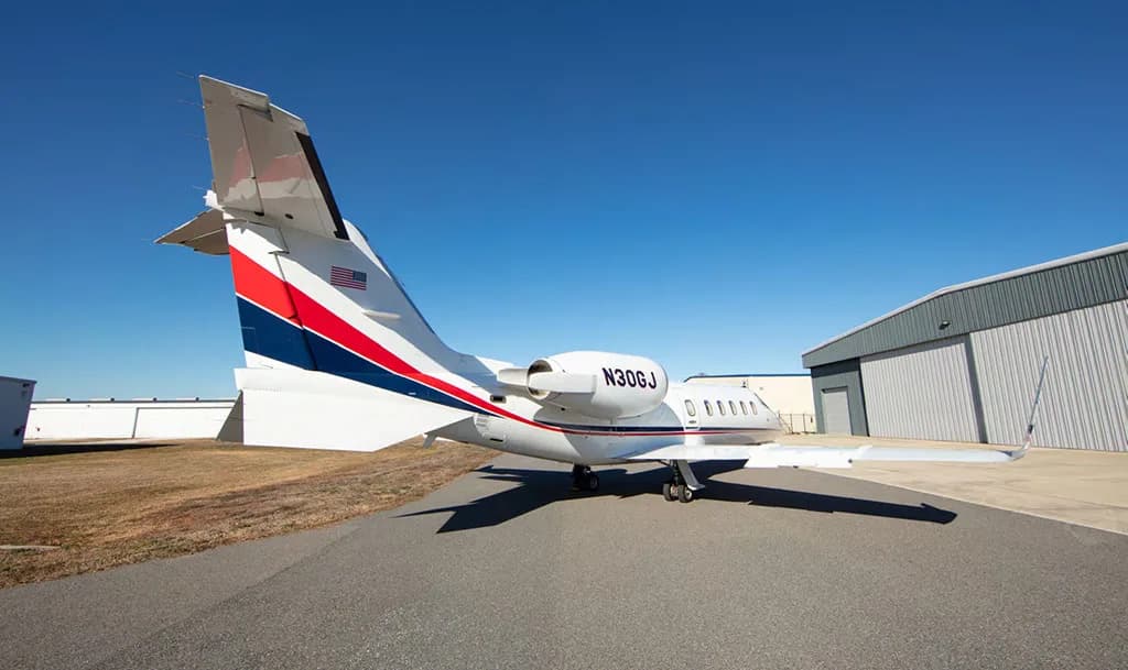Rear view of a white Learjet with red and blue tail stripes, registration N30GJ, parked on an airfield.