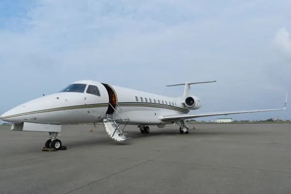 A white business jet with gold and black stripes is parked on an airfield with its main door open.