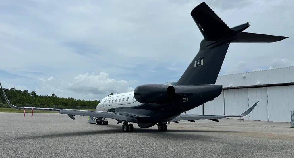 A rear view of a dark grey and white Embraer Praetor 600 business jet with a Canadian flag on the tail, parked on an airfield next to a hangar.