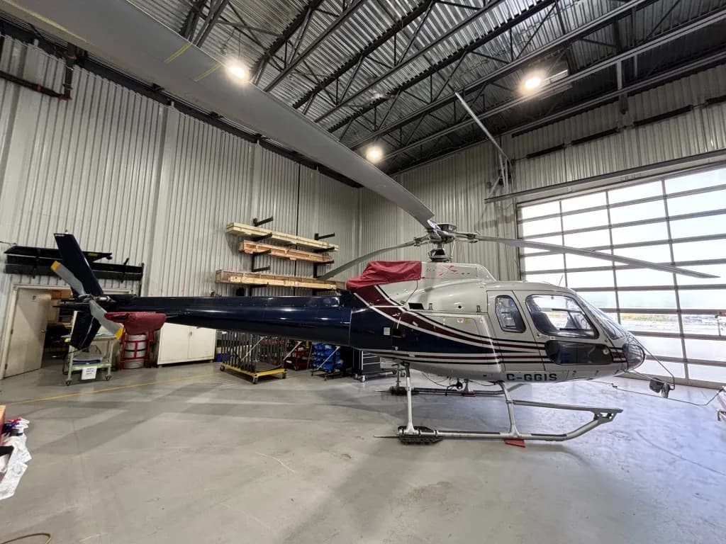 A silver and dark blue helicopter with red accents, registration C-GGIS, parked inside a hangar.