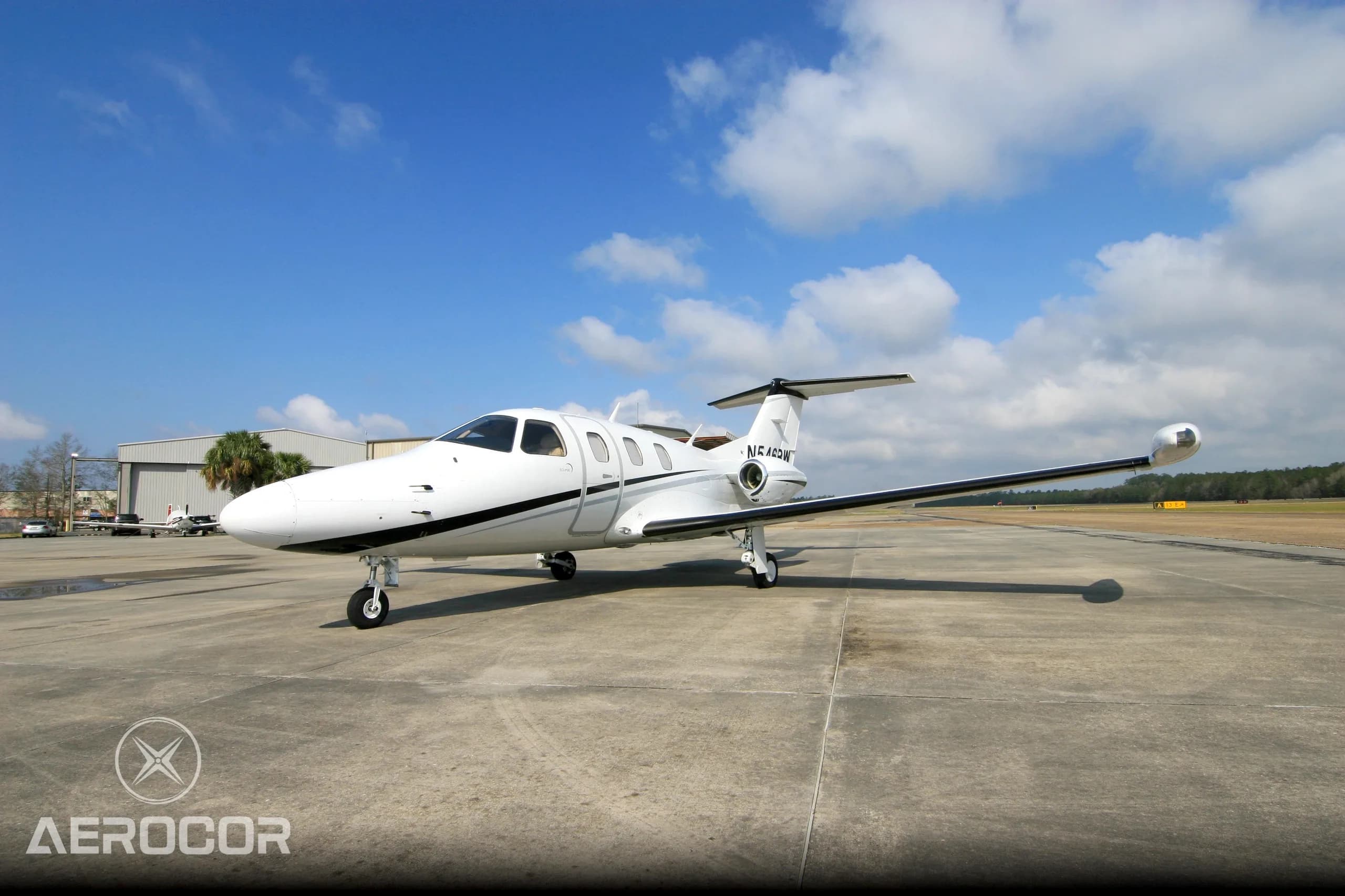 A white Eclipse 500 jet with black and grey stripes parked on an airfield under a blue sky.
