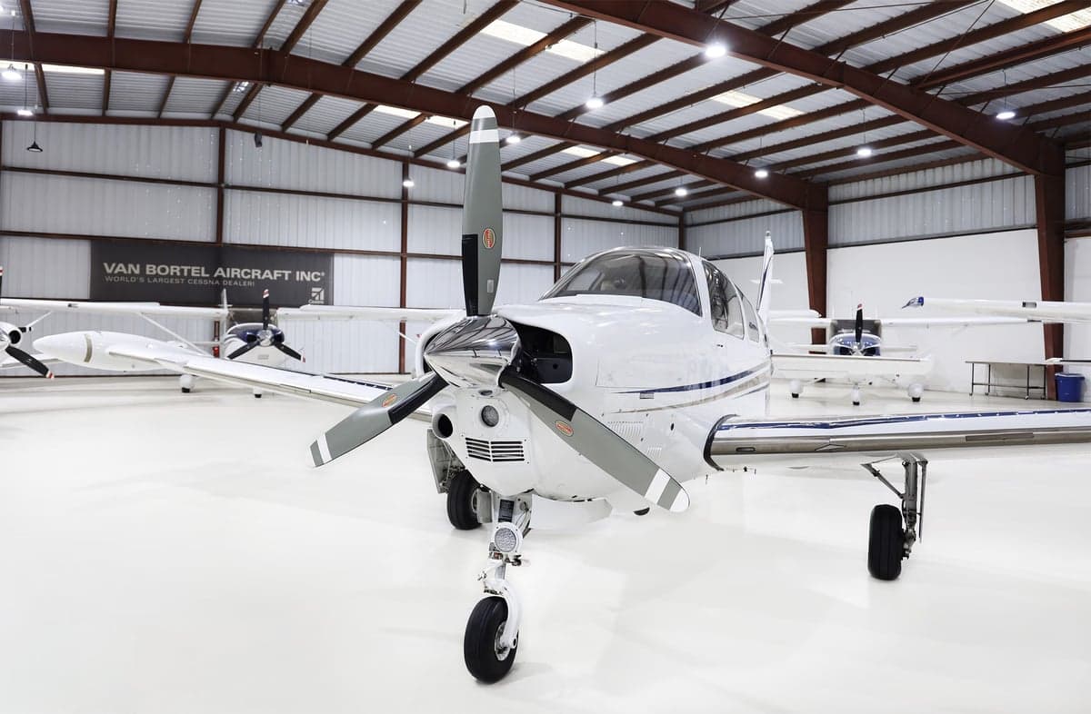 Front view of a white Beechcraft Bonanza N802PN with blue and grey stripes, parked in a hangar.