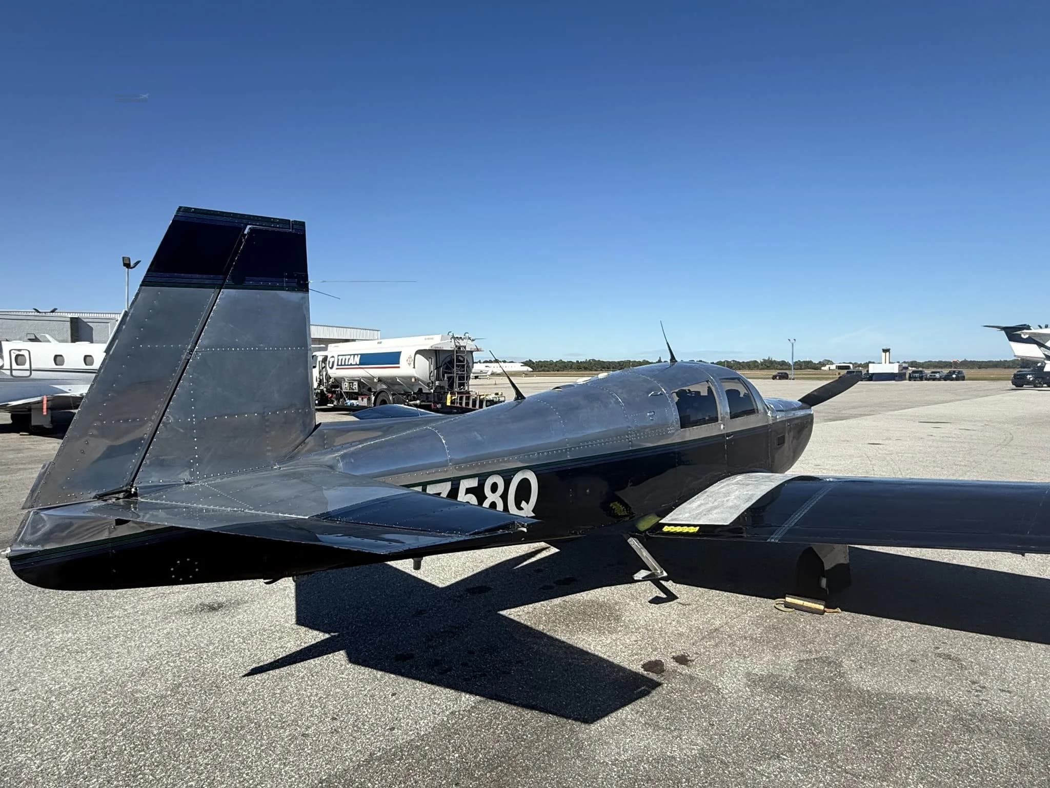 A black and silver Mooney M20 aircraft, N5758Q, parked on an asphalt tarmac with a fuel truck nearby.