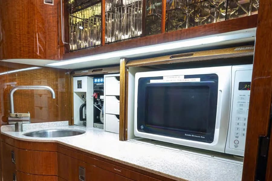 A close-up of the private jet's galley, showing a sink, a microwave oven, and dark wood cabinetry.
