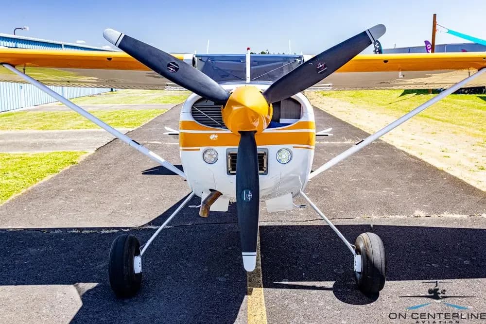 A head-on view of a white and orange Cessna 185 Skywagon (N1841R) with its propeller centered.