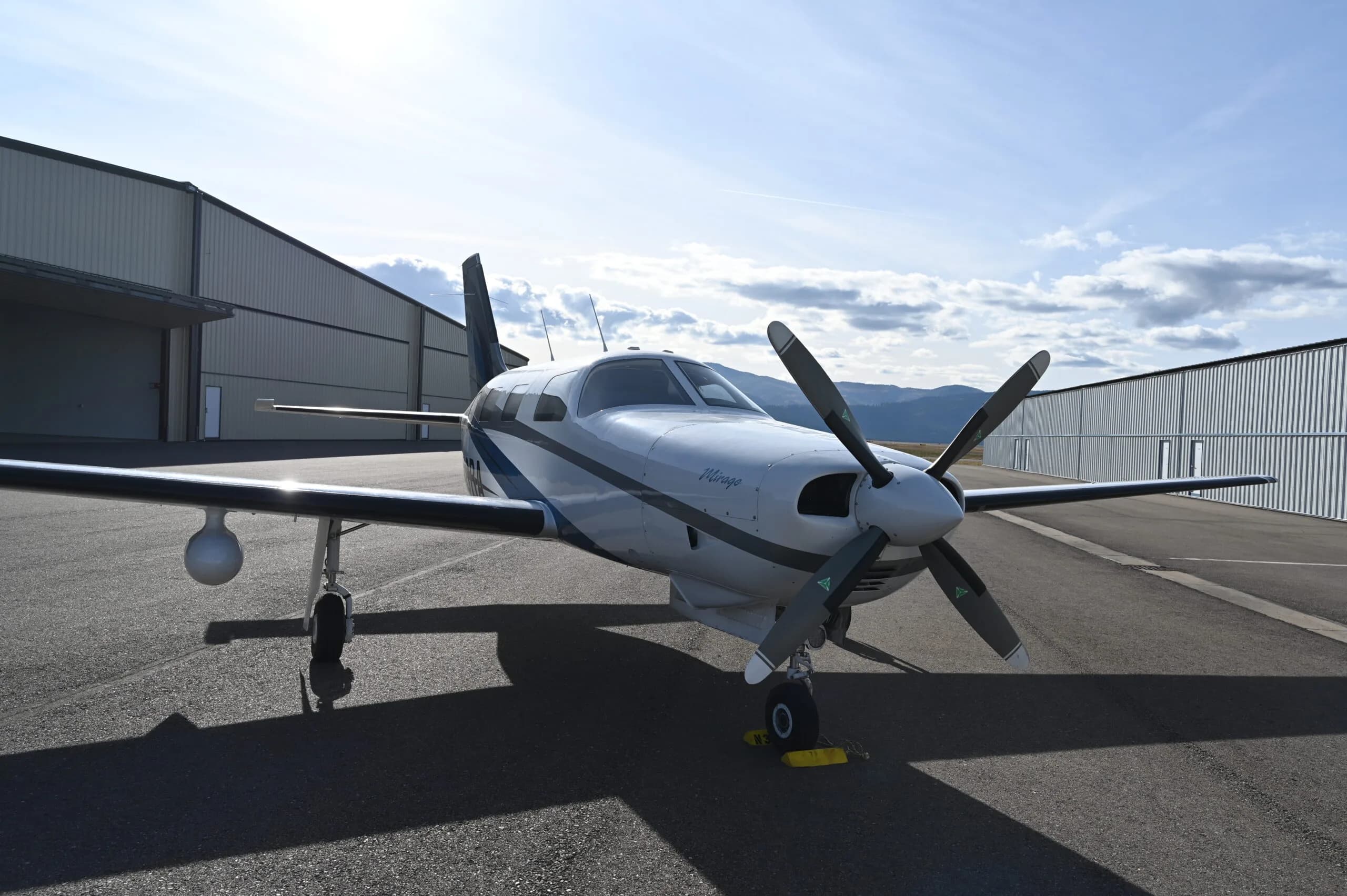 Front quarter view of a Piper Mirage parked on the tarmac in front of a hangar.