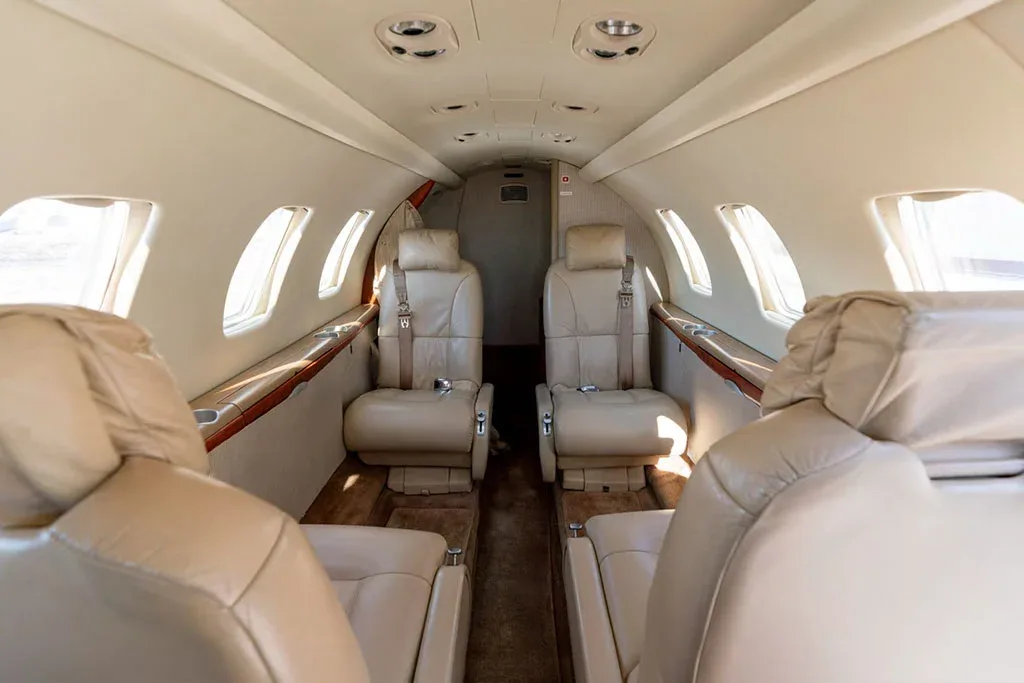 The interior cabin of a private jet, showing beige leather seats and the aisle looking towards the rear.
