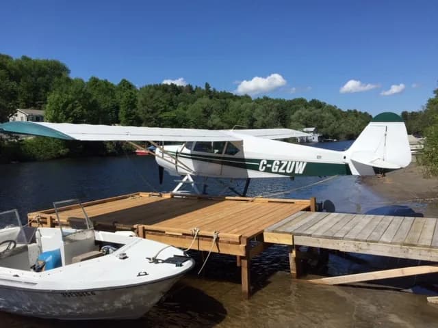 A white and green float plane, C-GZUW, is docked at a wooden pier on a lake.