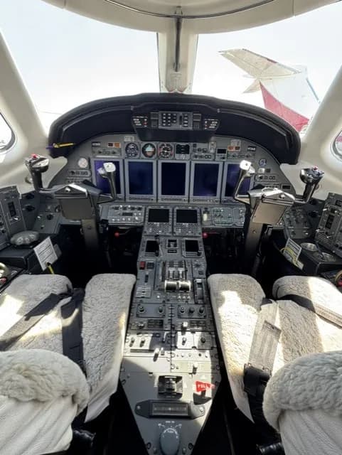 A detailed view of the business jet cockpit, showing the instrument panel, controls, and sheepskin seat covers.