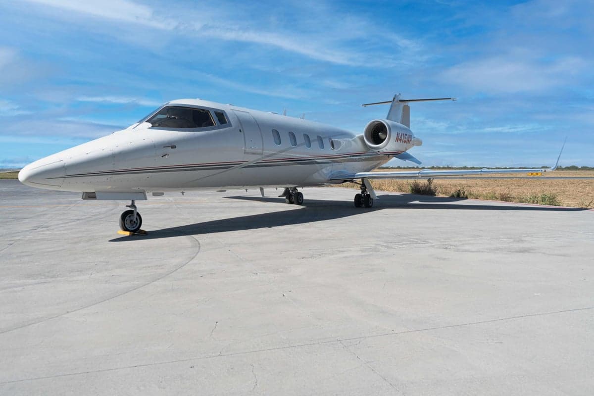 A white Learjet 45XR with registration N415NP is parked on the tarmac under a blue sky.