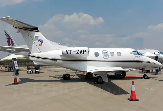 A white Embraer Phenom business jet with registration VT-ZAP on display outdoors under a blue sky.