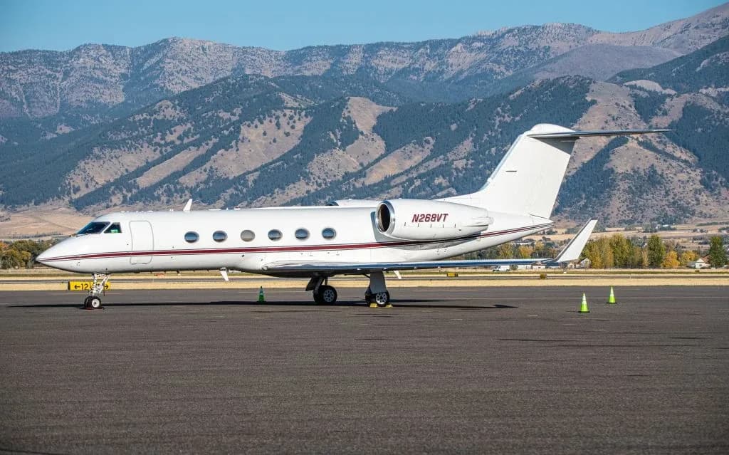 Gulfstream jet with red accents parked on the tarmac with mountains in the background.