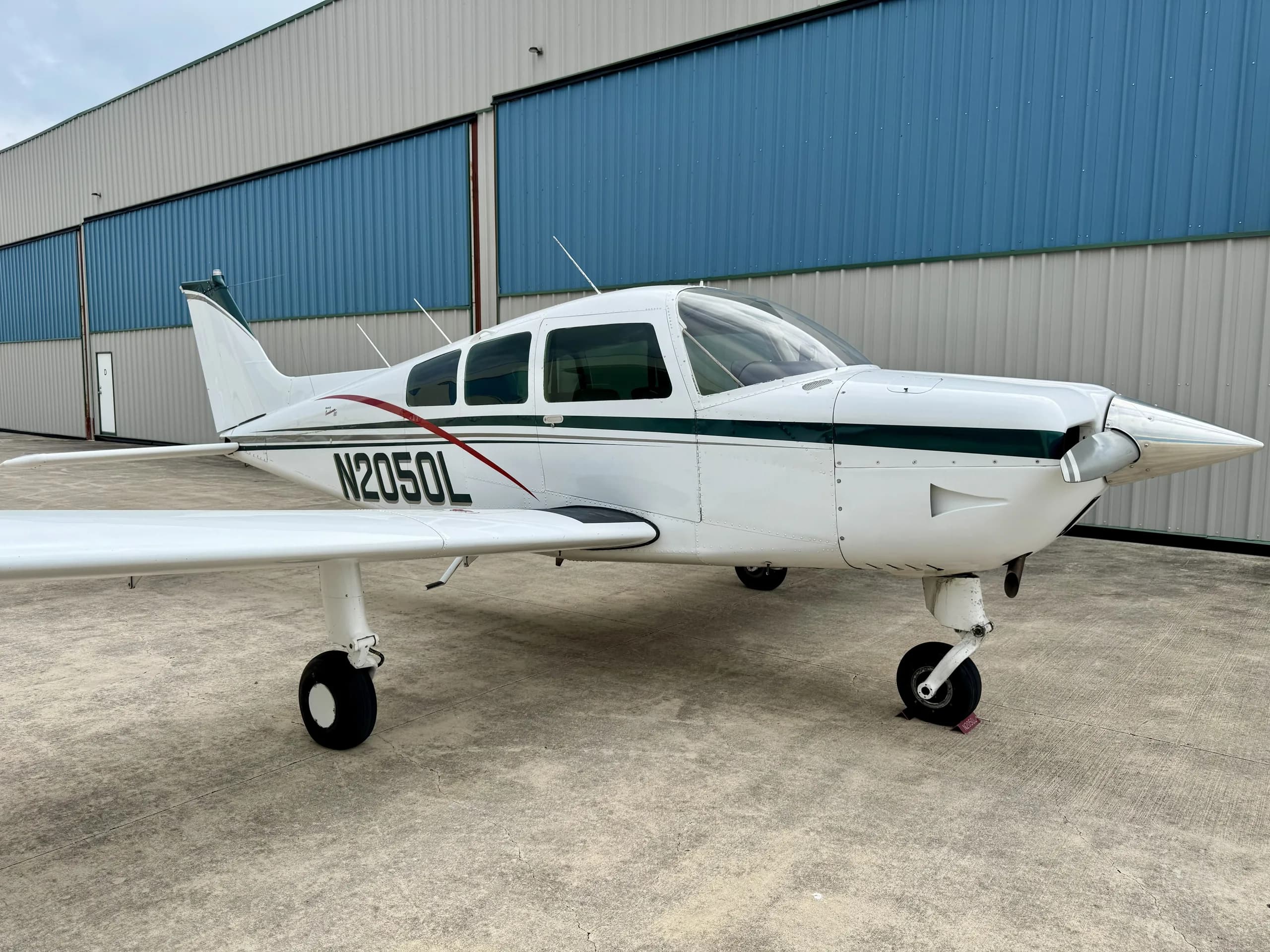 Front three-quarter view of a white and green Beechcraft Sundowner N2050L parked on concrete.