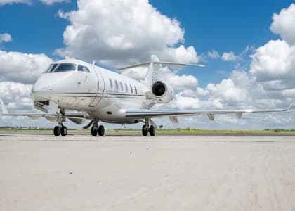A white Bombardier Global Express business jet is parked on the tarmac under a blue sky with fluffy white clouds.