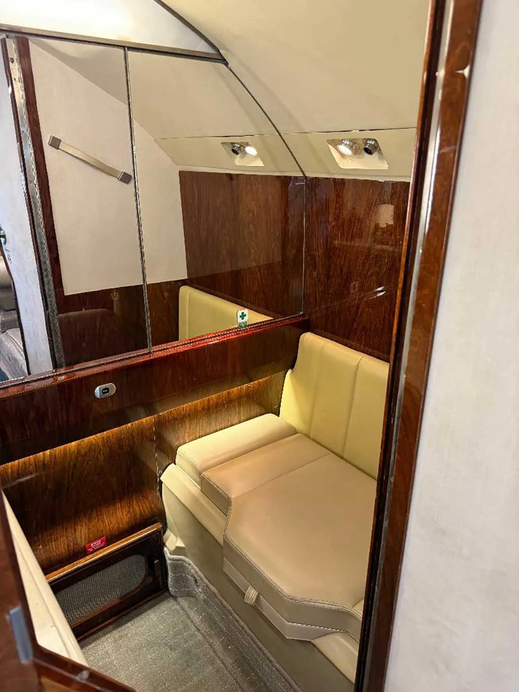 A small seating area within the aircraft's interior, featuring tan upholstery, polished wood, and mirrored walls.