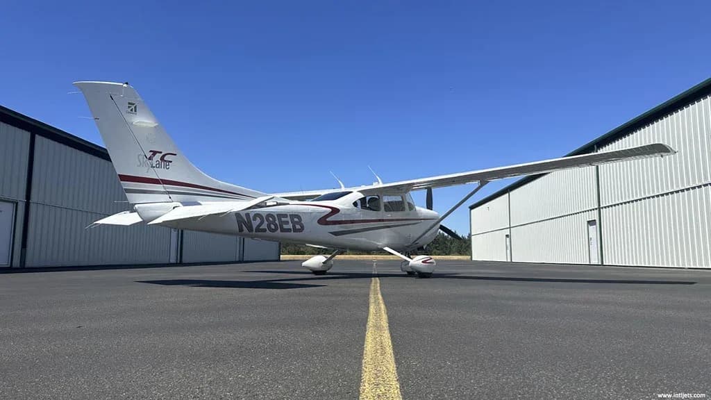 A white Cessna 182 Skylane with red and gray stripes, registration N28EB, parked on an asphalt ramp with a yellow centerline.