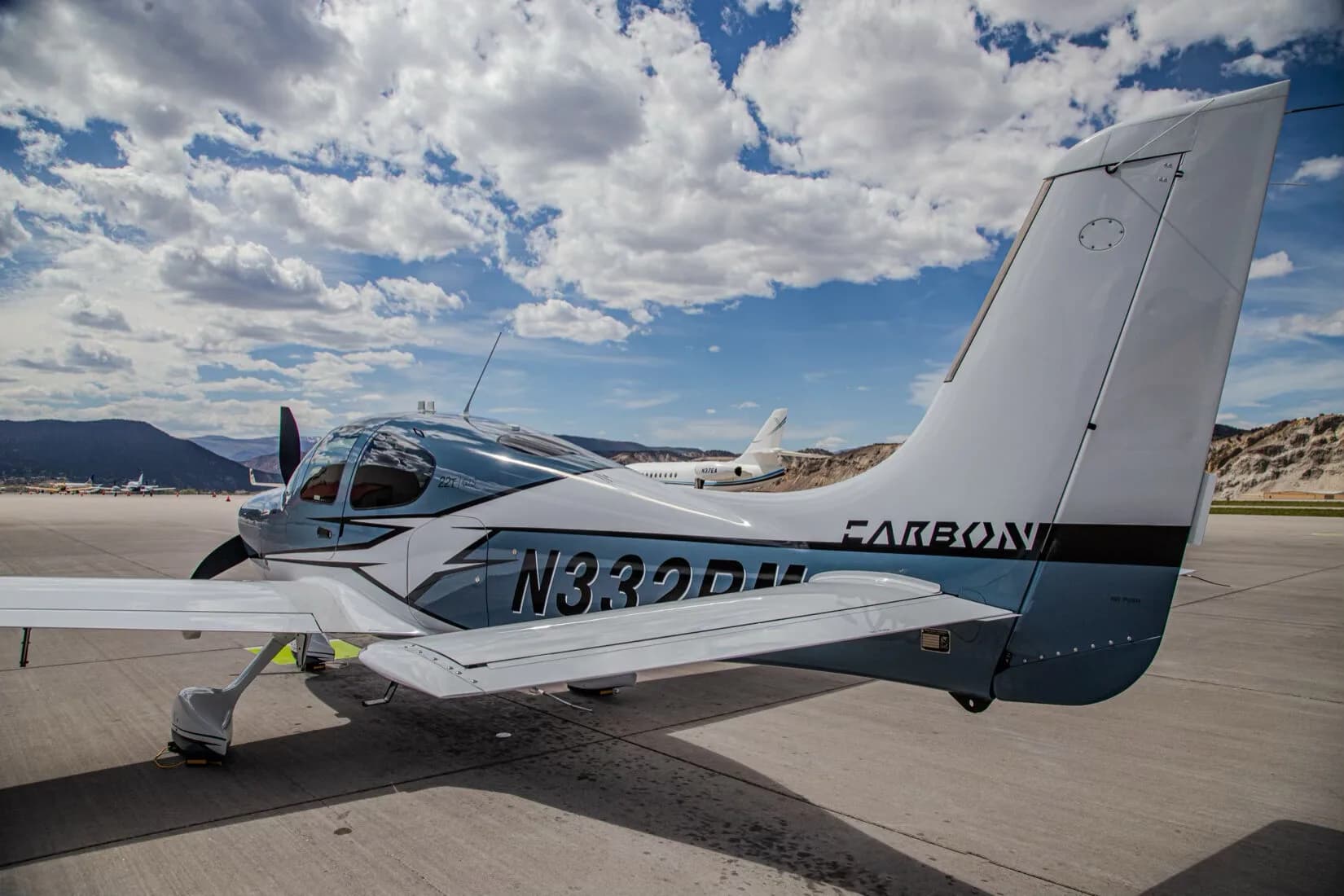 Rear-side view of a blue and white Cirrus SR22T GTS aircraft, registration N332RM, parked on an airport tarmac.