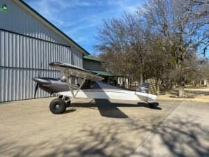 A Carbon Cub aircraft is parked on a concrete pad in front of a building.