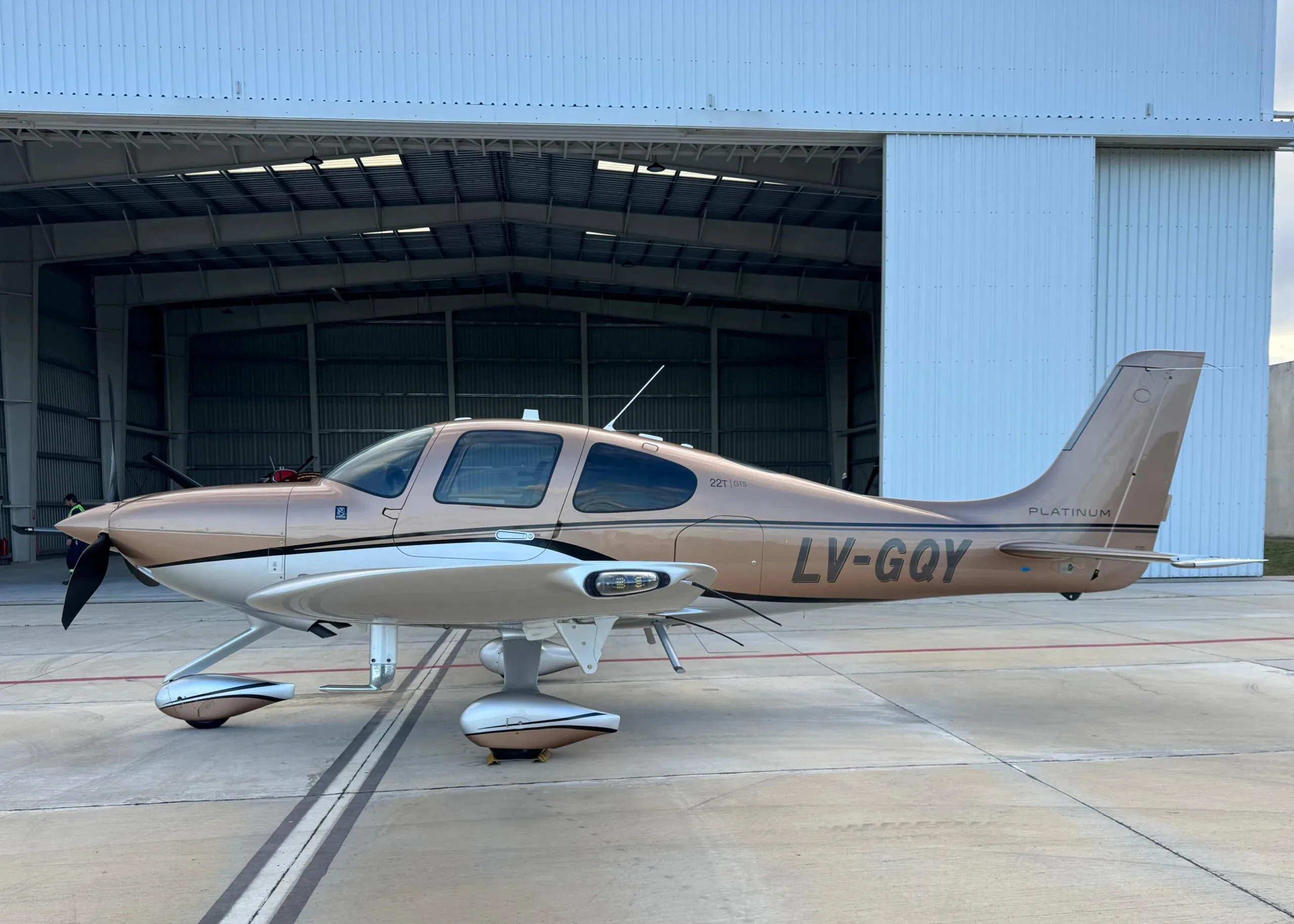 A brown and silver Cirrus SR22T aircraft with registration LV-GQY parked in front of an open hangar.