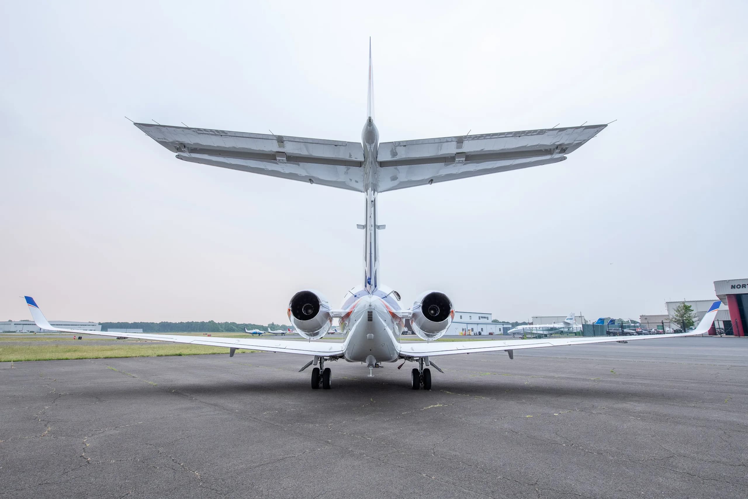 A white business jet with blue and orange stripes on the tarmac, viewed from directly behind.