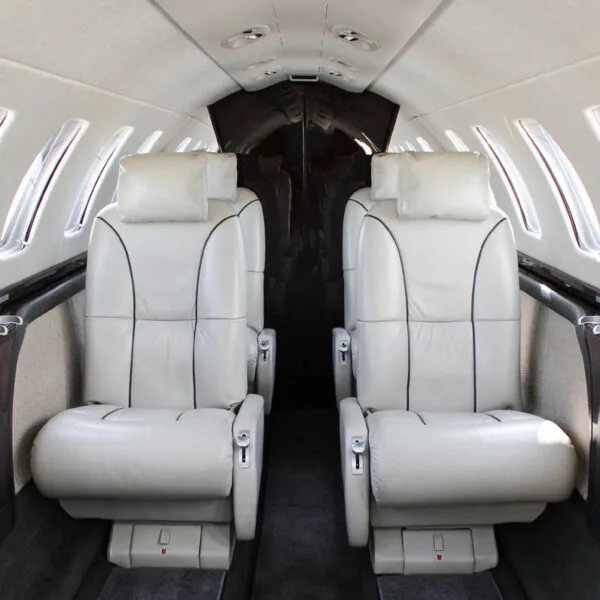 View of the aircraft cabin looking aft, showing two rows of light-colored leather seats.
