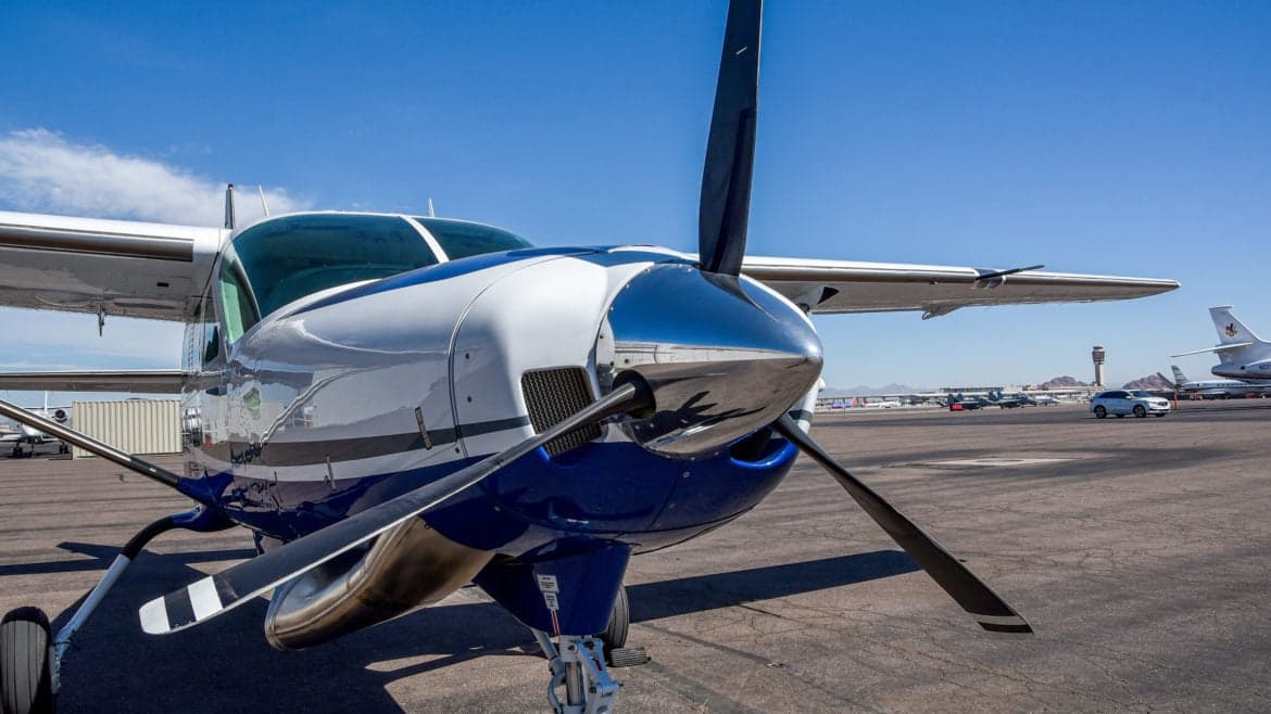 Close up of the front of a Cessna Caravan on the tarmac with a control tower in the background.