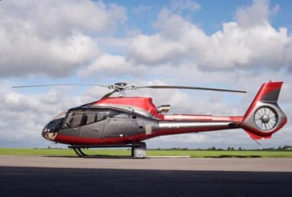 A red and gray helicopter sits on a runway under a cloudy sky.