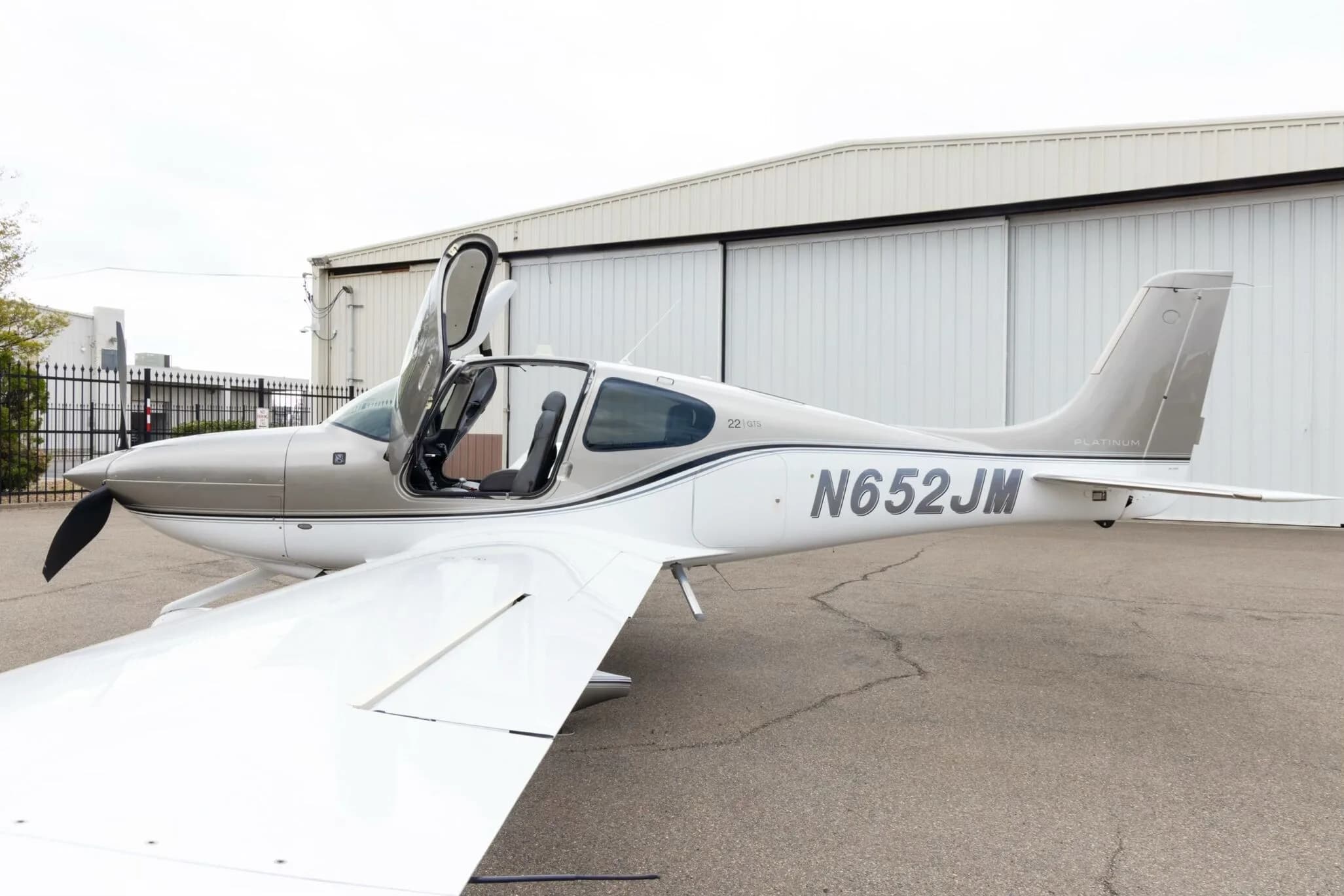 A side view of the silver and white Cirrus SR22 aircraft with N652JM registration, showing the pilot's side gull-wing door open.