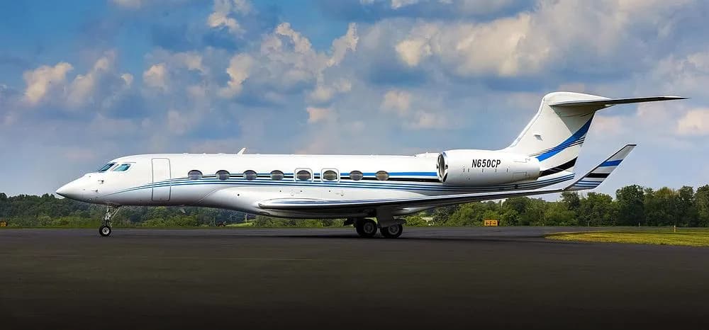 A white Gulfstream G650 business jet with blue and black stripes and registration N650CP parked on an tarmac.