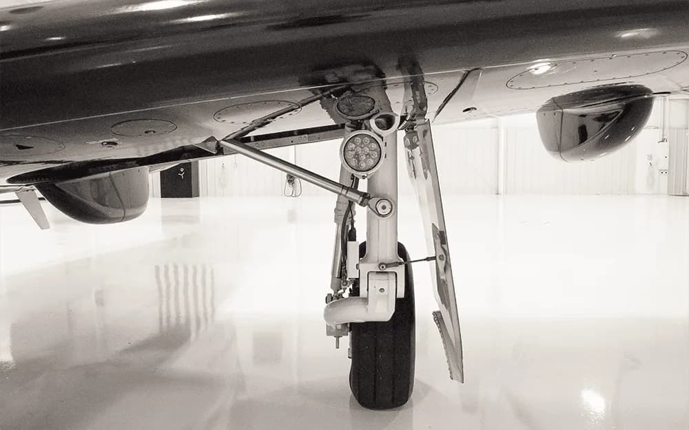 Black and white close-up of the main landing gear and undercarriage of a Pilatus PC-12 aircraft.