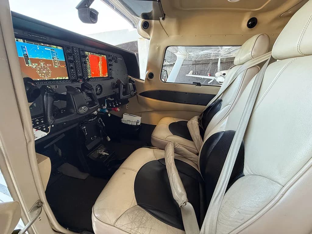 The aircraft's tan and black leather interior cabin, with a view towards the cockpit's glass panel displays.