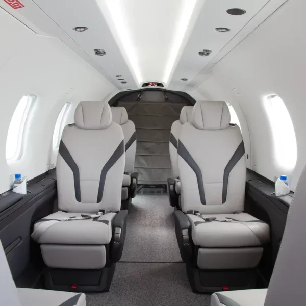 A modern aircraft cabin interior with grey and black two-tone leather seats and overhead lighting.