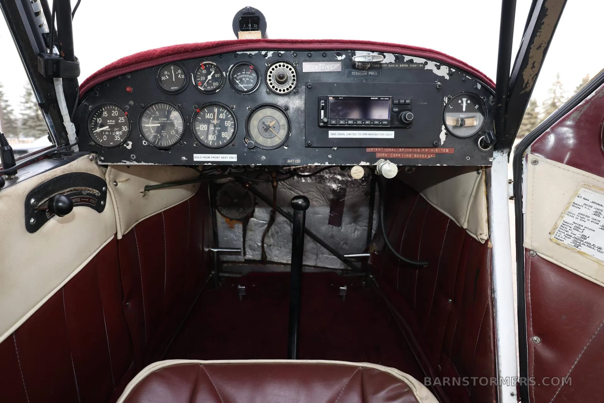 The cockpit of the aircraft, showing a classic instrument panel with analog gauges, a modern radio, and a red upholstered seat.