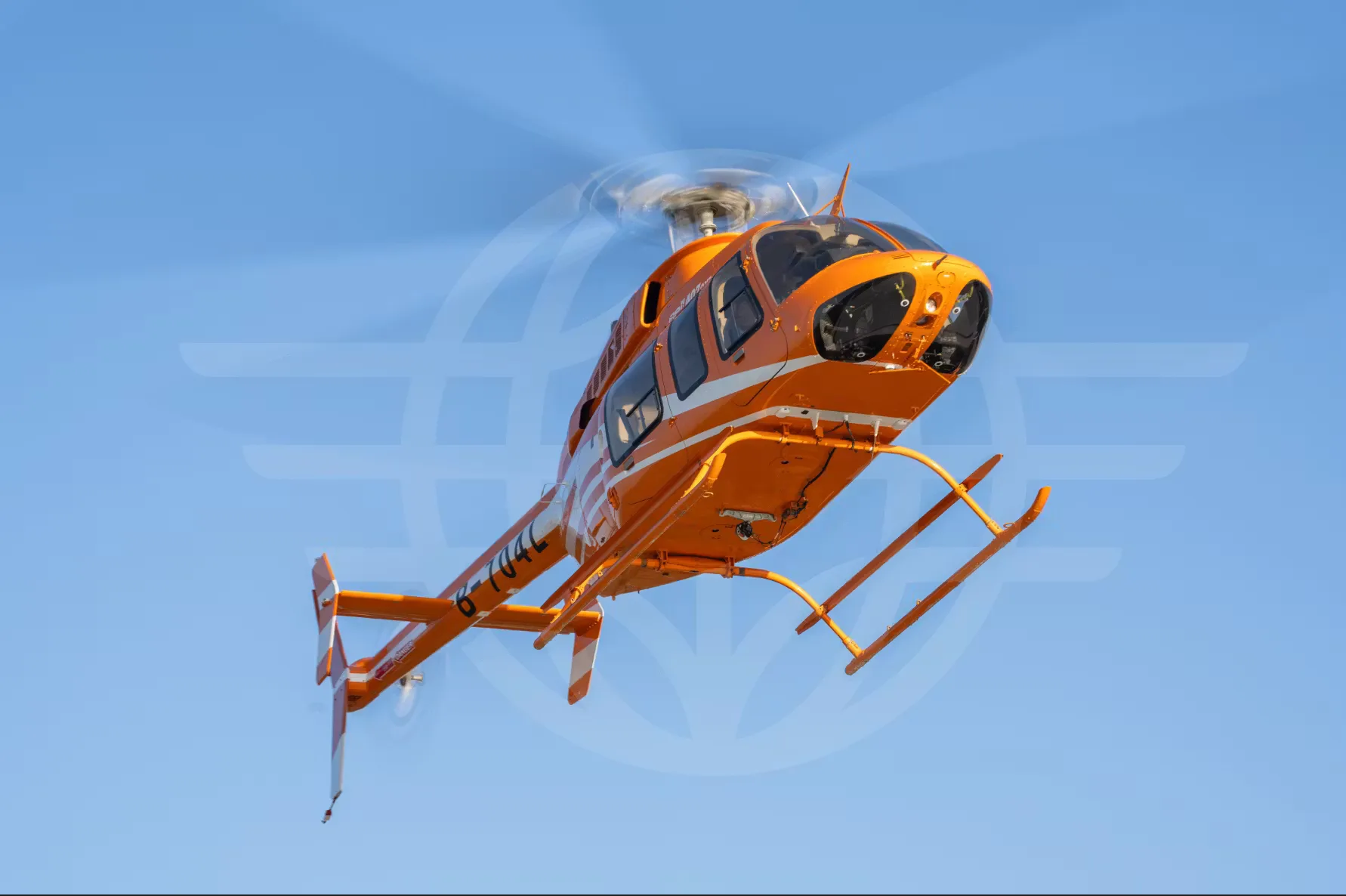 An orange and white Bell 407GXi helicopter is in flight against a light blue sky.