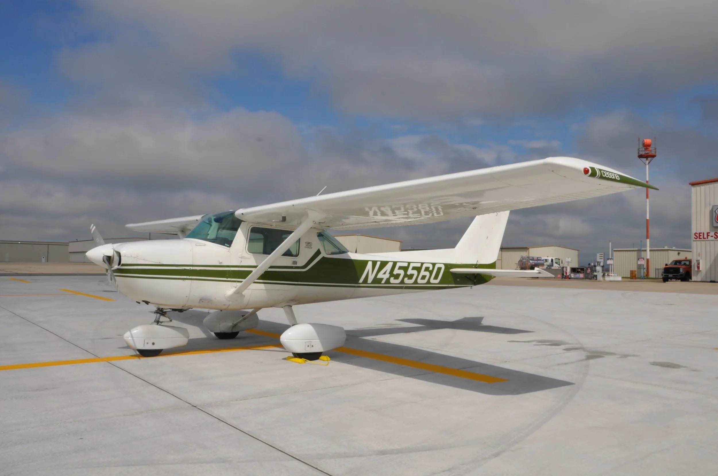 A white and green Cessna N45560 aircraft is parked on an airfield under a cloudy sky, viewed from a slightly front-side angle.