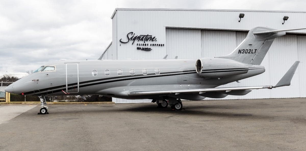 Side view of the aircraft N302LT parked in front of a Signature Flight Support hangar.