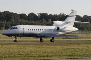 Side view of a white and gray Falcon jet on the ground.